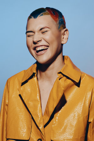 smiling woman with colorful short hair wearing a bright yellow jacket, joyful expression, studio...
