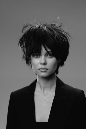 Black and white portrait of a young woman with short hair wearing a black blazer looking serious.