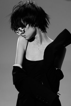 Black and white portrait of a stylish woman with short hair wearing a black dress, expressing...