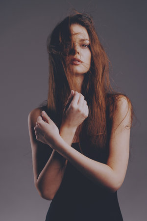 Melancholic woman with long hair in black dress with subdued lighting and muted background