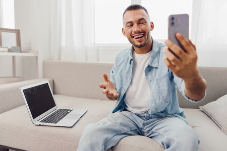 Smiling man engaged in a video call, dressed casually, showcasing modern home office setup. Bright and inviting atmosphere promotes connection and productivity.の写真素材