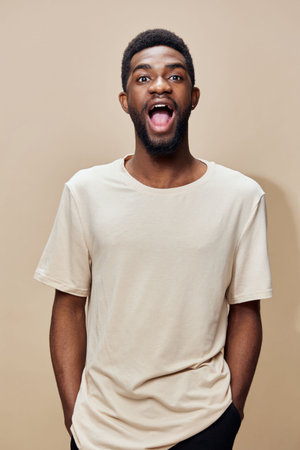 Excited young Black man expressing joy in a light beige t shirt against a neutral background,...