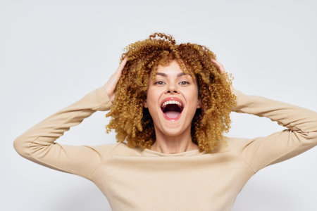 joyful woman with curly hair expressing happiness, casual outfit, light background, vibrant and cheerful concept Smiling and energetic pose highlights positivity and joy in lifeの写真素材