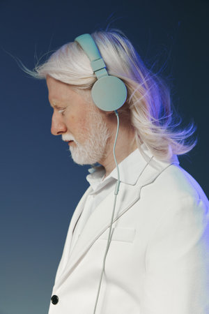 Elderly man with long white hair wearing pastel blue headphones, side profile against a gradient...