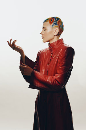Woman with colorful short hair wearing a red leather jacket poses confidently against a bright neutral background in a modern fashion portrait.の写真素材
