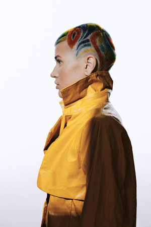 woman with colorful short hair and creative shaved design, wearing yellow jacket, profile portrait, modern fashion and artistic hairstyle in studio lightingの写真素材