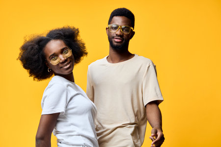 Happy Black couple with curly hair wearing casual outfits and glasses against a vibrant yellow background, showcasing joy and connection in a colorful settingの写真素材