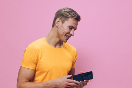 Smiling man holding smartphone, casual yellow t-shirt, happy expression, looking at device, isolated...