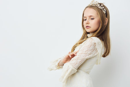 Elegant girl in a white dress with a crown, showcasing confidence and grace against a soft white background, perfect for themes of beauty and innocenceの写真素材