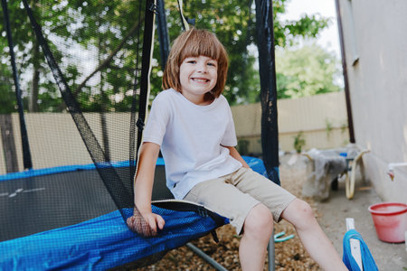 Smiling boy enjoying playful moments on a trampoline, surrounded by greenery and a cheerful atmosphere, perfect for capturing childhood joy and fun.の写真素材