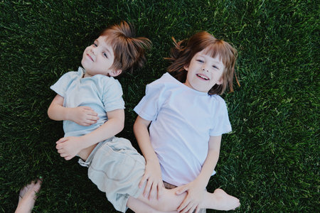 Happy children lying on green grass, enjoying a sunny day filled with laughter and joy. This playful scene captures the essence of childhood moments beautifully.の写真素材