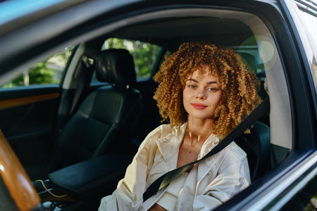 smiling woman with curly hair wearing white jacket sitting in car seatbelt fastened on sunny day...