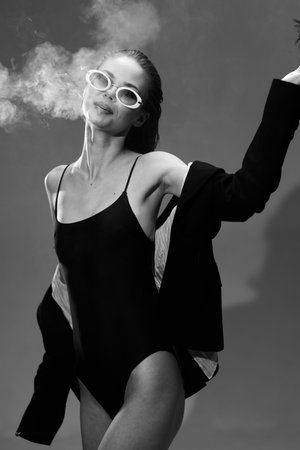 Stylish woman wearing sunglasses and black swimsuit with smoke around her in black and whiteの写真素材