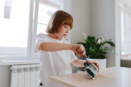 Curious young boy engaging with a toy robot, using a screwdriver in a bright and cheerful indoor environment, showcasing creativity and exploration.の写真素材