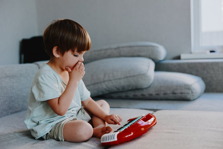 Curious boy playing with a toy keyboard, exploring sounds and music, enjoying a moment of creativity and imagination while seated on a comfortable couch.の写真素材
