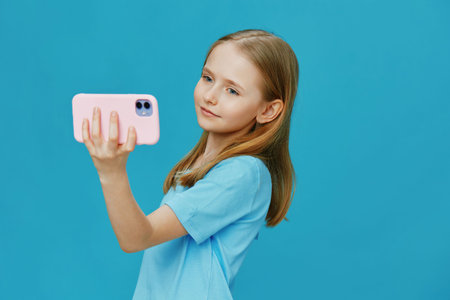 Cute girl taking a selfie against a blue background, showcasing joy and confidence in casual attire...