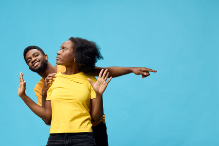 Happy diverse couple posing against a blue background, showcasing playful interaction and vibrant yellow outfits, perfect for joy and diversity themesの写真素材