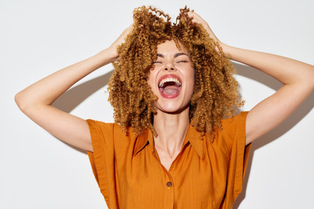 Happy woman with curly hair expressing joy and excitement against a white background, showcasing positivity and energy through her vibrant pose and bright clothingの写真素材