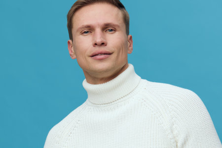 Close-up of a man with short blond hair wearing a white turtleneck sweater against a blue...