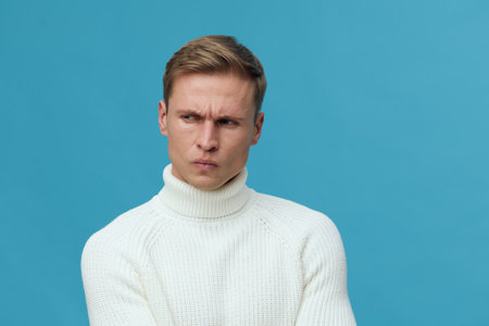 thoughtful man wearing white turtleneck sweater against blue background focused look communication conceptの写真素材