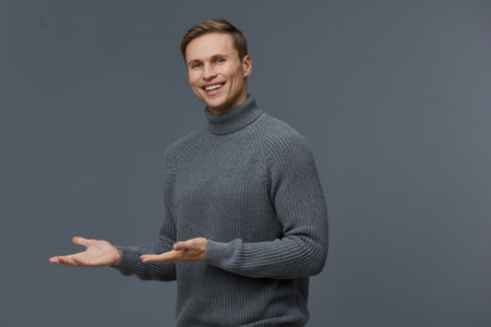 smiling caucasian man in gray sweater present gesture digital nomad casual wear isolated gray background studio portraitの写真素材