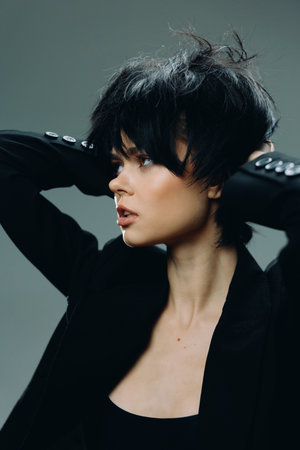 Stylish woman with short black hair in a black jacket posing against a dark background, showcasing modern fashion and confident expression.の写真素材