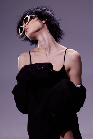 Stylish woman in sunglasses wearing black clothing with a modern short haircut posing confidently on a gray background.の写真素材