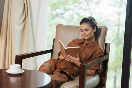 A young woman of mixed ethnicity reading a book in a cozy armchair, wearing a stylish brown outfit,...