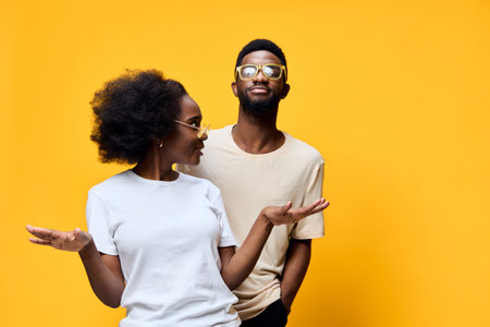 Stylish African couple in casual outfits expressing joy against a bright yellow background, perfect for lifestyle and fashion themesの写真素材