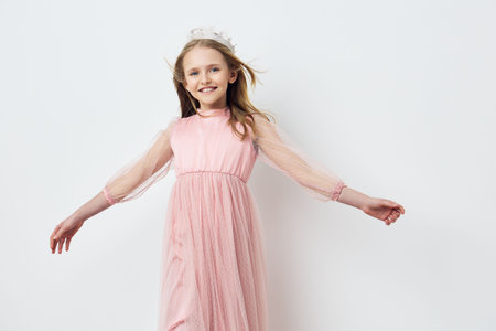 Happy girl in a pink dress with flowing sleeves, joyfully spinning with a smile, against a soft white background Perfect for children s fashion themes and joyful momentsの写真素材