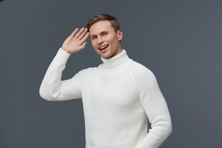 smiling man wearing white sweater waving hand gesture isolated on gray background video call digital nomad concept cheerful young caucasian personの写真素材