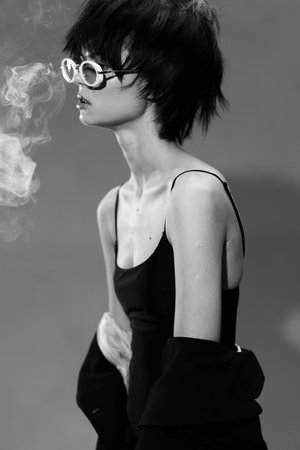 Black and white portrait of a young woman with short hair wearing sunglasses exhaling smoke with a stylish look.の写真素材
