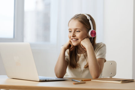Smiling girl with headphones enjoying online learning at home, bright atmosphere, cozy interior with...