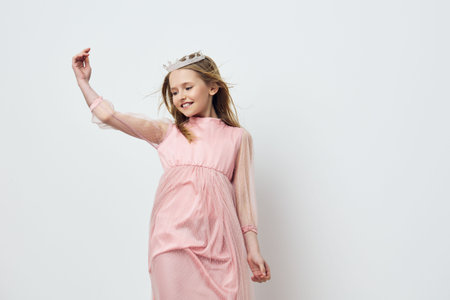 Cheerful girl in pink dress with crown, enjoying playful moment in studio, symbolizing innocence and...