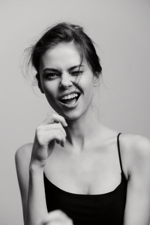 Playful woman with a charming smile winking at the camera, dressed in a simple black top, showcasing a lighthearted and fun attitude. Joy and spontaneity concept.の写真素材