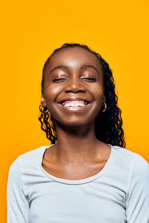 Happy African girl with curly hair smiling brightly against a vibrant yellow background, showcasing joy and positivityの写真素材