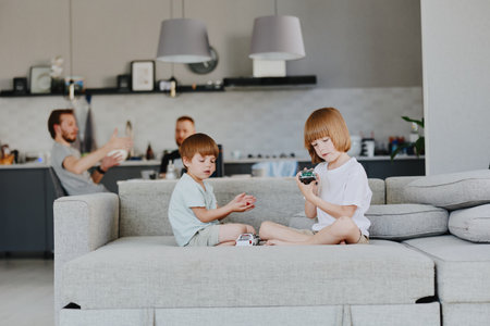 Two children playing together on a sofa in a modern living room, while a man is interacting in the background. A cozy family atmosphere is present, fostering connection.の写真素材