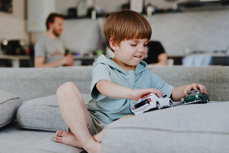 Happy boy playing with toy cars at home, showcasing creativity and imagination while engaging in joyful playtime with family members in the background.の写真素材