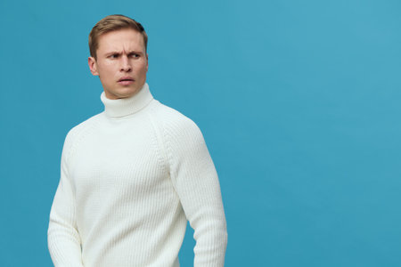 serious young caucasian man wear white turtleneck sweater looking side near blue wall studio portrait man working digital nomad conceptの写真素材