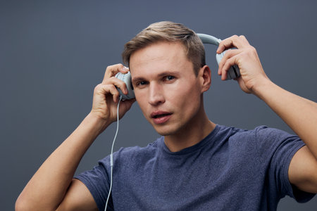 Young man wearing headphones listening to music with focused expression isolated on gray background digital detox mental health conceptの写真素材