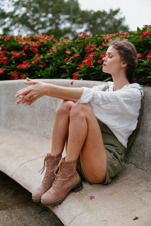 Young woman in a casual outfit sitting outdoors among blooming flowers, expressing tranquility in a nature inspired setting, perfect for seasonal lifestyle themesの写真素材