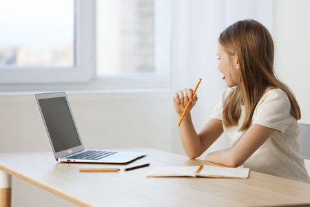 Young girl pondering while studying at home, with laptop and stationery, conveying concentration and...