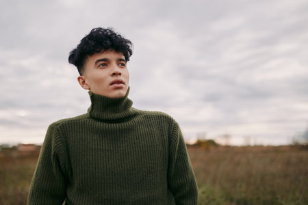 A young man in a green turtleneck stands in an open field, portrait captures an authentic, credible...