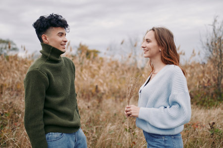 Two young adults stand in a windswept field, sharing a warm, candid conversation that highlights...