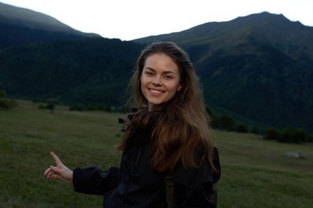 A cheerful young woman stands in an open field with distant mountains, smiling at the camera and radiating confidence against a natural, scenic backdrop.の写真素材