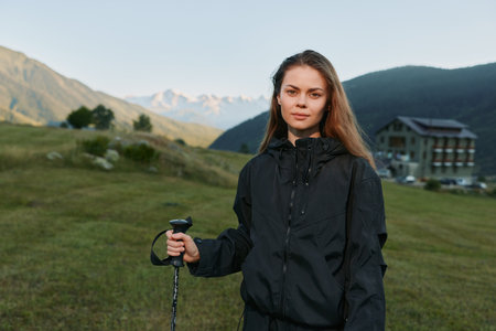A focused hiker stands outdoors in a scenic alpine landscape, holding a trekking pole and wearing a...