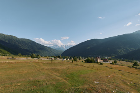A peaceful rural landscape with rolling fields, distant mountains, a small village, and a bright...