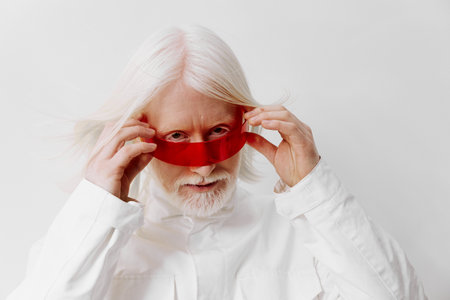Creative man with long white hair wearing a red accessory against a light background, showcasing a...