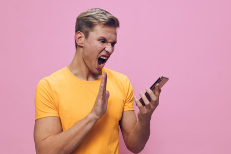 angry man wearing yellow t-shirt scream hold smartphone frustrated cyber security concept isolated...
