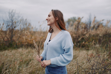 [Young woman smiling in a windswept field captured in an authentic, genuine moment of quiet joy;...